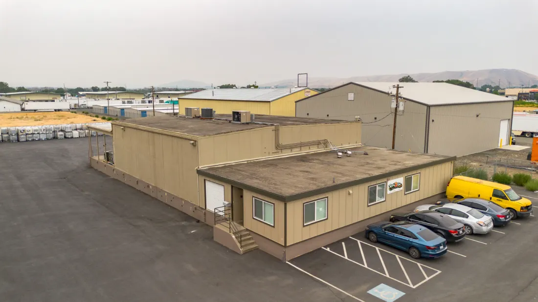 Aerial drone view of the Ready 2 Go wholesale warehouse in Yakima, WA, main office trailer with parking, warehouse buildings behind, Rattlesnake Hills on the horizon
